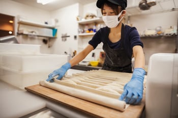 woman-working-in-a-bakery-wearing-protective-glove-WDFLCEM